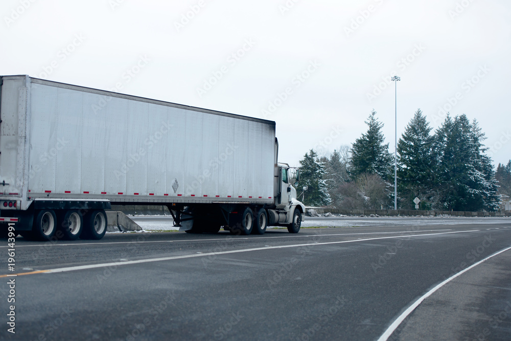 Big rig semi truck with dry van semi trailer running in snow storm winter weather on the interstate road