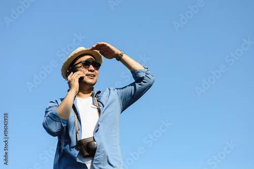Tourist Asian man talking mobile phone with blue sky in summer.