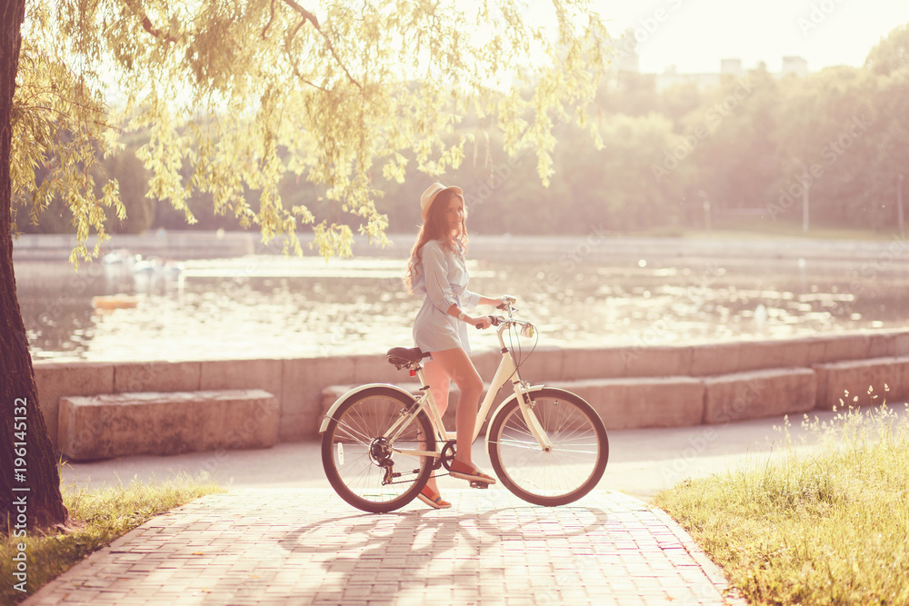 Obraz premium portrait of a beautiful girl in a hat with a bicycle on city background in the sunlight