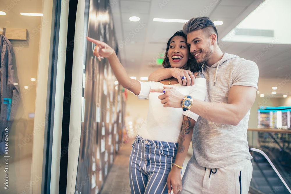 Young happy couple looking at a window of a clothing store in shopping mall Young happy couple looking at a window of a clothing store in shopping mall