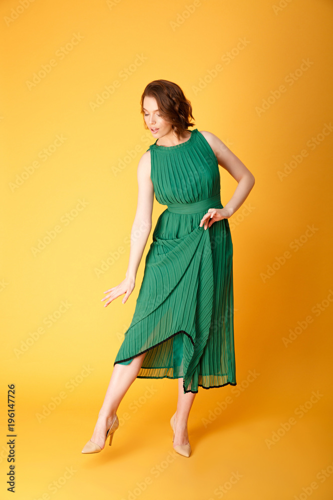 beautiful woman in green dress looking at shoe isolated on orange beautiful woman in green dress looking at shoe isolated on orange