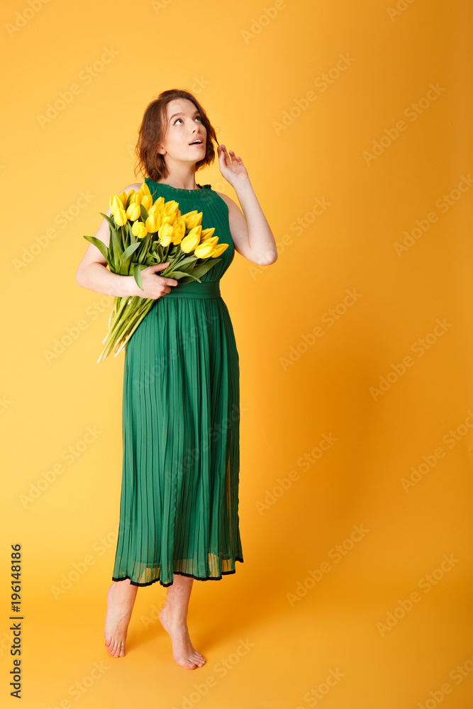 pensive woman in green dress with bouquet of yellow tulips isolated on orange pensive woman in green dress with bouquet of yellow tulips isolated on orange
