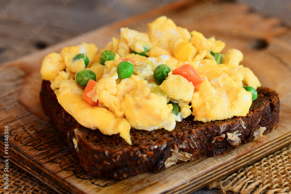 Scrambled eggs with vegetables on rye bread. Soft scrambled egg omelette. Homemade cuisine. Rustic stile. Closeup Scrambled eggs with vegetables on rye bread. Soft scrambled egg omelette. Homemade cuisine. Rustic stile. Closeup