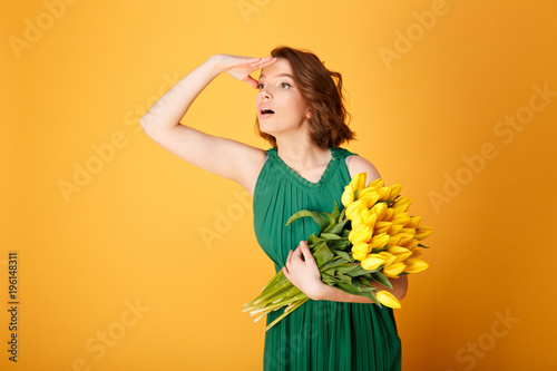 portrait of young woman with bouquet of yellow tulips looking away isolated on orange
