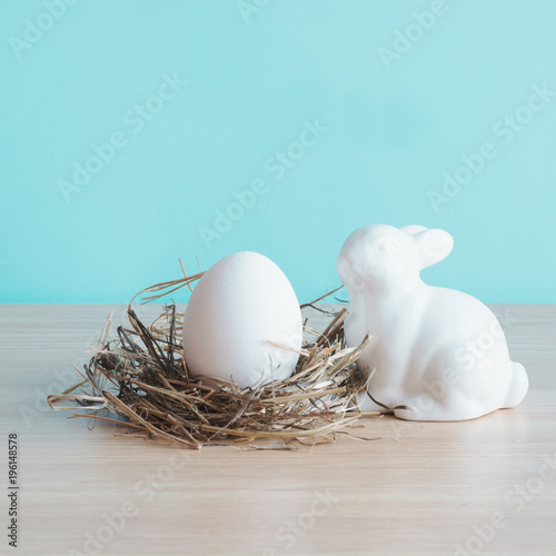 White egg in the nest and rabbit on wooden board. Easter composition.