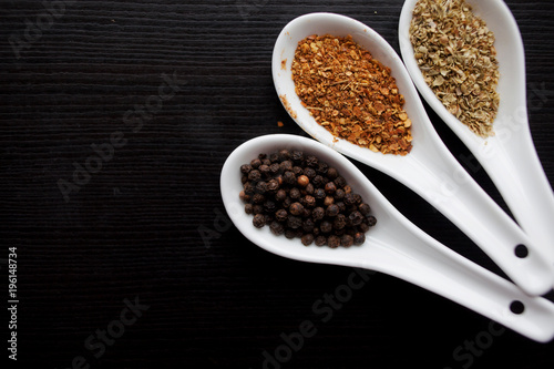 Black and red pepper, set of spices in spoons. On black wooden table