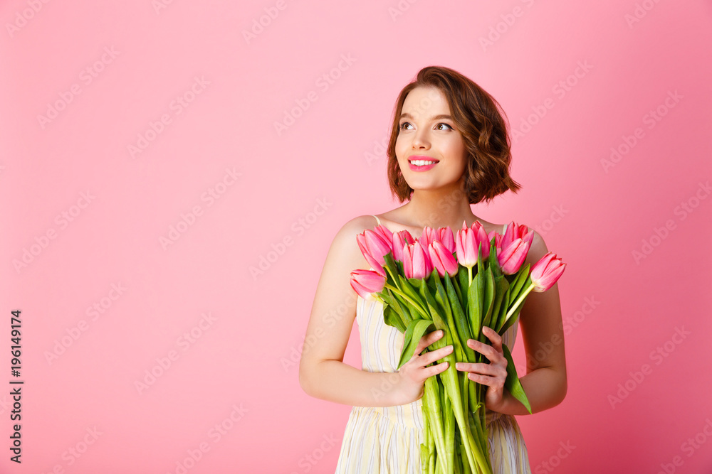 smiling woman with bouquet of pink tulips looking away isolated on pink