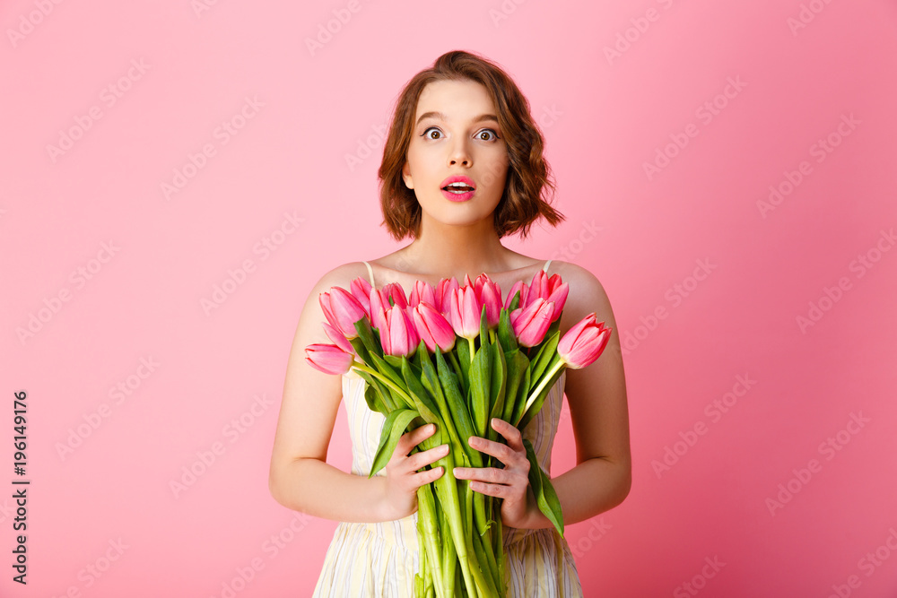 shocked young woman with bouquet of pink tulips looking at camera isolated on pink shocked young woman with bouquet of pink tulips looking at camera isolated on pink