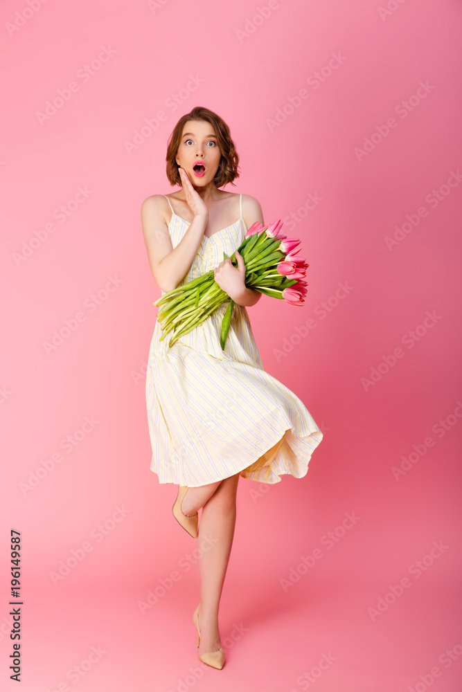 young shocked woman with bouquet of pink tulips looking at camera isolated on pink young shocked woman with bouquet of pink tulips looking at camera isolated on pink