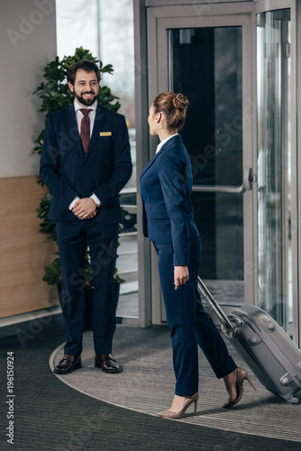 businesswoman going out of hotel luggage and looking at doorman photo