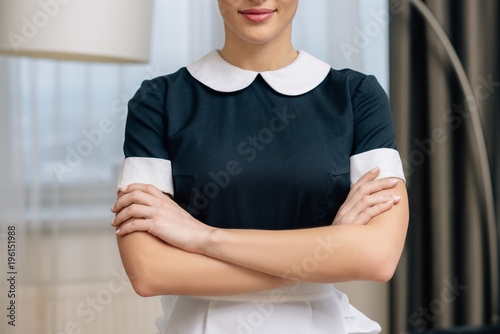 cropped shot of smiling maid in uniform with crossed arms photo