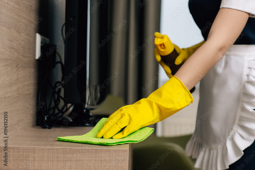 cropped shot of maid in uniform wiping shelf with rag and aerosol furniture cleaner cropped shot of maid in uniform wiping shelf with rag and aerosol furniture cleaner