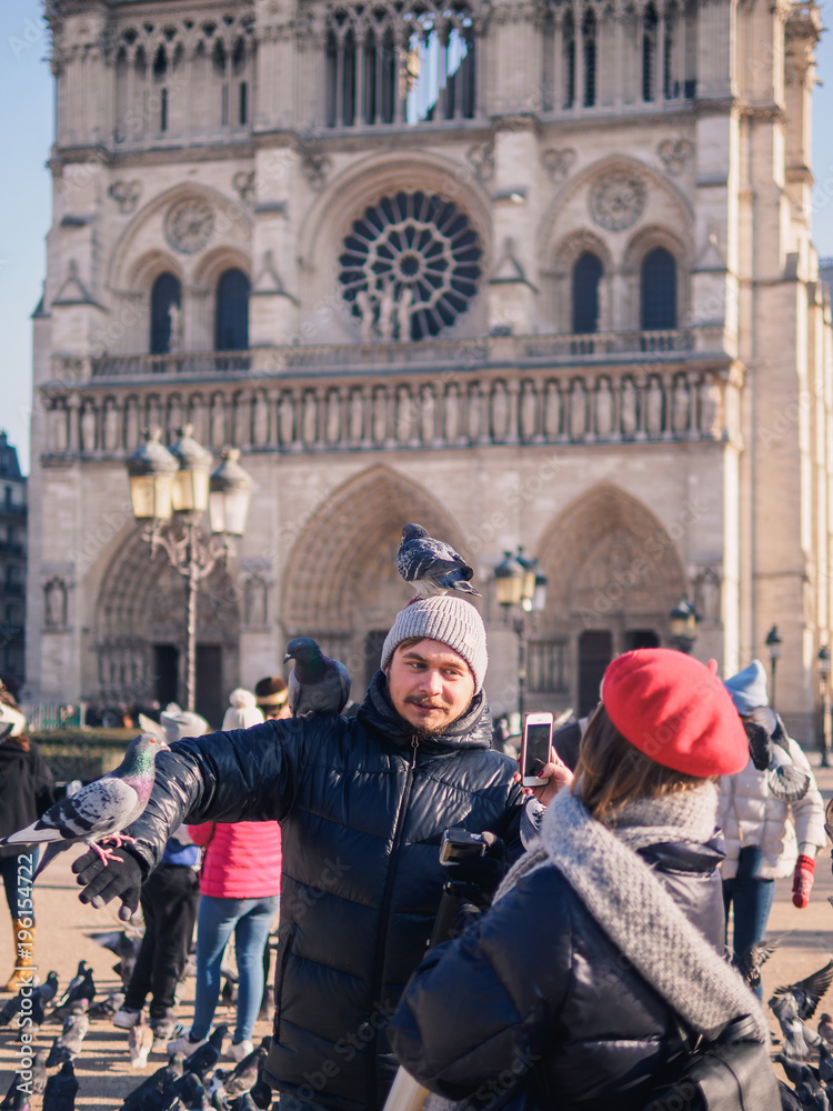 Tourists feeding pigeons in the square in front of the cathedral of Notre Dame