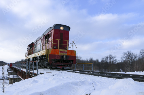Shunting locomotive to ride on the railway bridge in winter. The locomotive is moving along the snow railway. Winter trip by train.