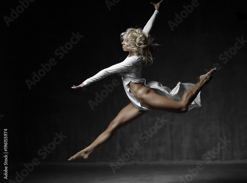 Amazing sexy blonde woman in white dress with beautiful sporty muscle body doing a split jump.