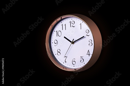 Close up of a Large Decorative ticking wall clock in metallic rose gold color and white face, accurate time as it is fitted with a quartz, Isolated object on black background