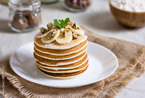 Stack of delicious pancakes with chocolate, honey, nuts and slices of banana and stawderry jam on plate and napkin on wooden background