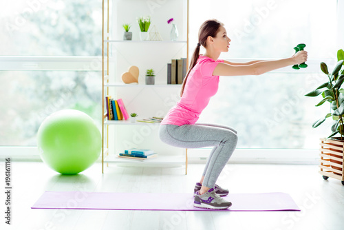 Profile view photo of focused strong concentrated enduring beautiful gorgeous stylish trendy girl dressed tight leggings casual tshirt doing sit-ups holding green dumbbells in hands white light room