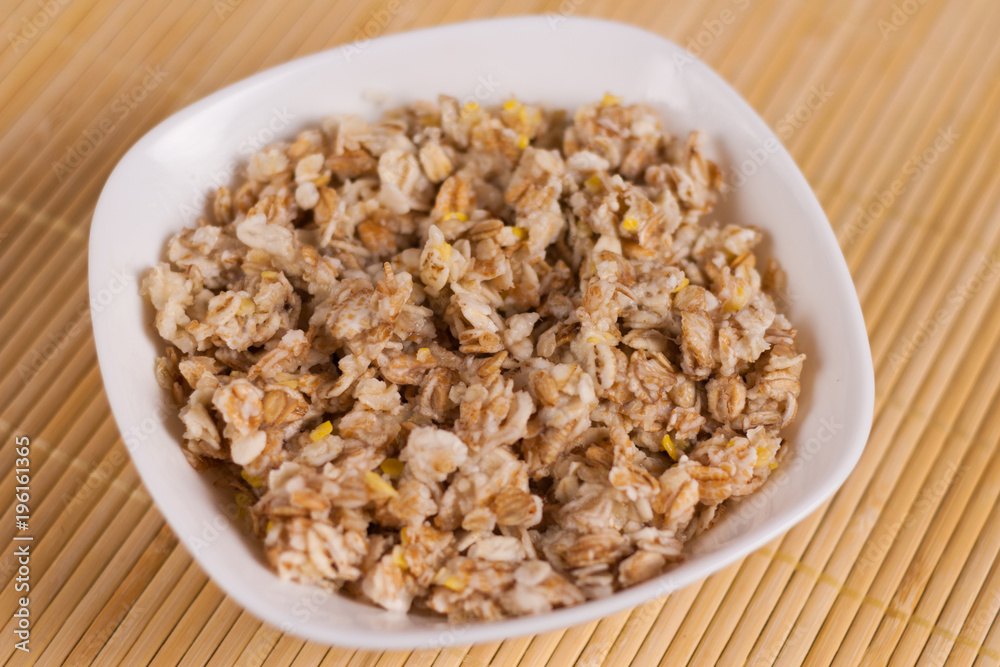 Cooked yummy warm oatmeal in white ceramic bowl on clean bamboo rug