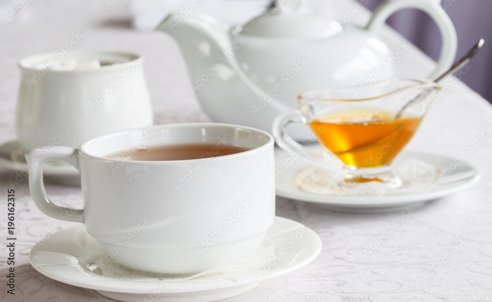 White cup of tea with honey on a white background with teapot. Serving tea. Honey in Saucer.