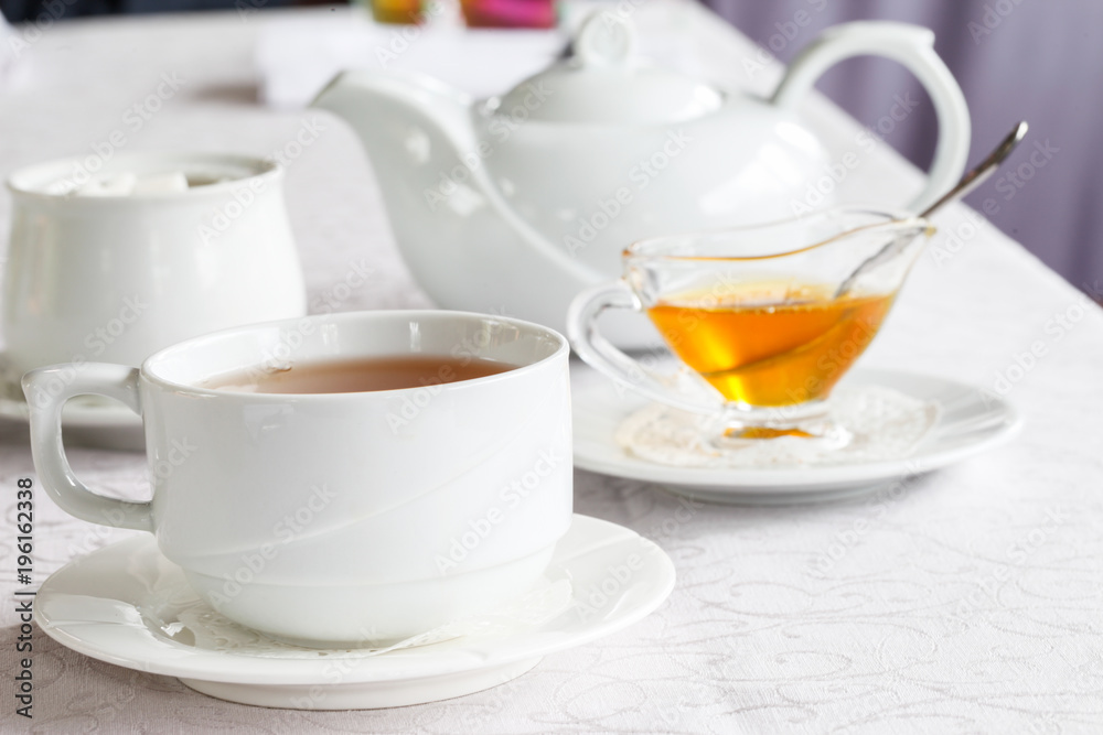 White cup of tea with honey on a white background with teapot. Serving tea. Honey in Saucer. White cup of tea with honey on a white background with teapot. Serving tea. Honey in Saucer.