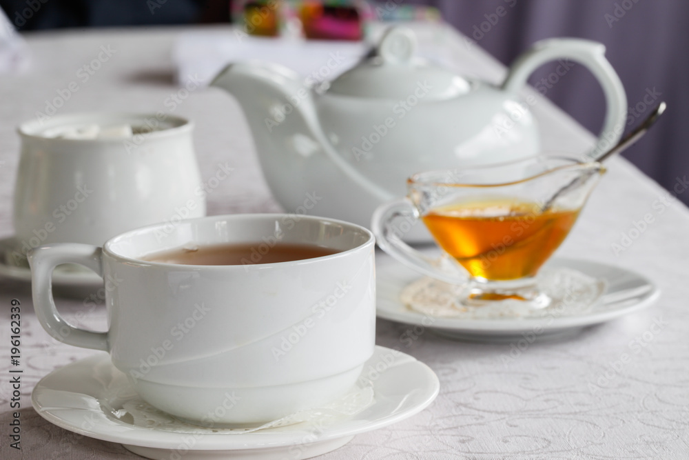 White cup of tea with honey on a white background with teapot. Serving tea. Honey in Saucer. White cup of tea with honey on a white background with teapot. Serving tea. Honey in Saucer.