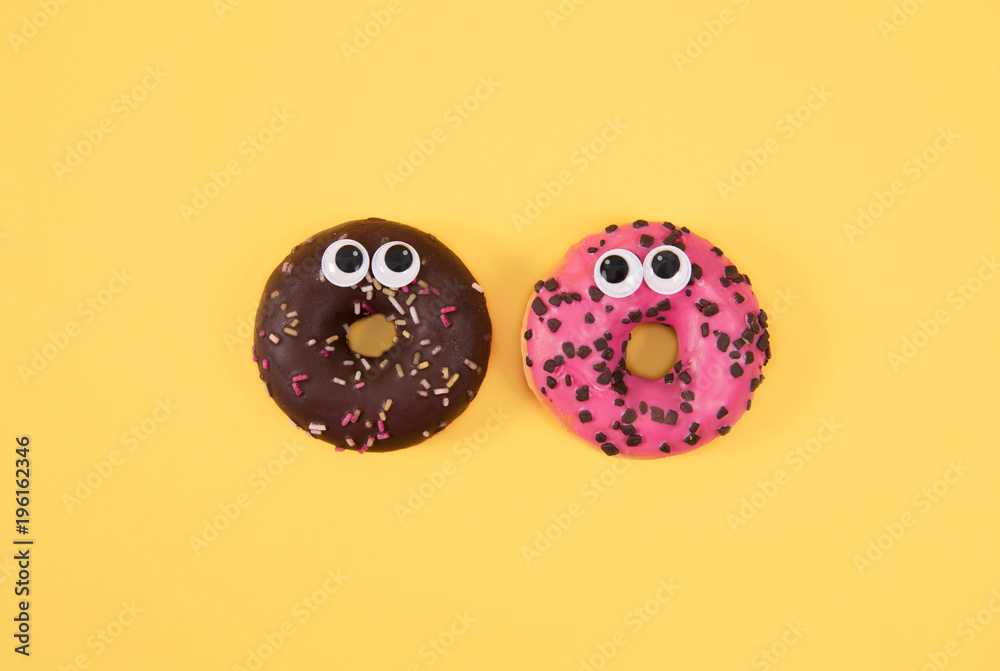Colorful glazed donuts with funny eyes on yellow background.