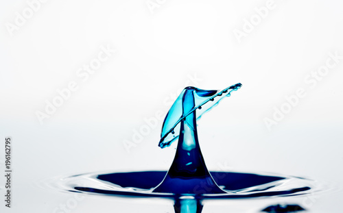 Splash and crown on rippled blue liquid or water surface . Water splash with a crown and reflection