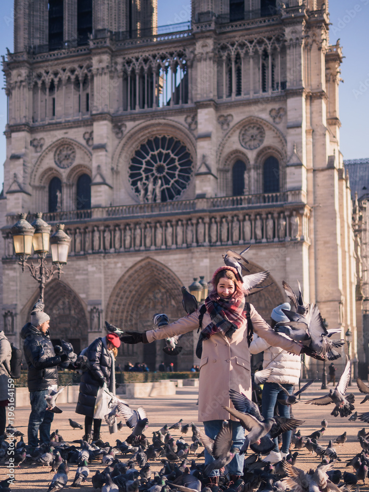 Tourists feeding pigeons in the square in front of the cathedral of Notre Dame