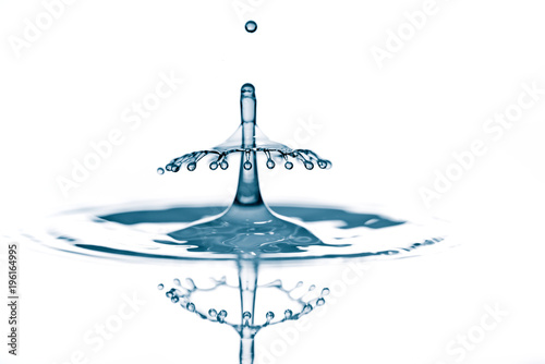 Splash and crown on rippled blue liquid or water surface . Water splash with a crown and reflection