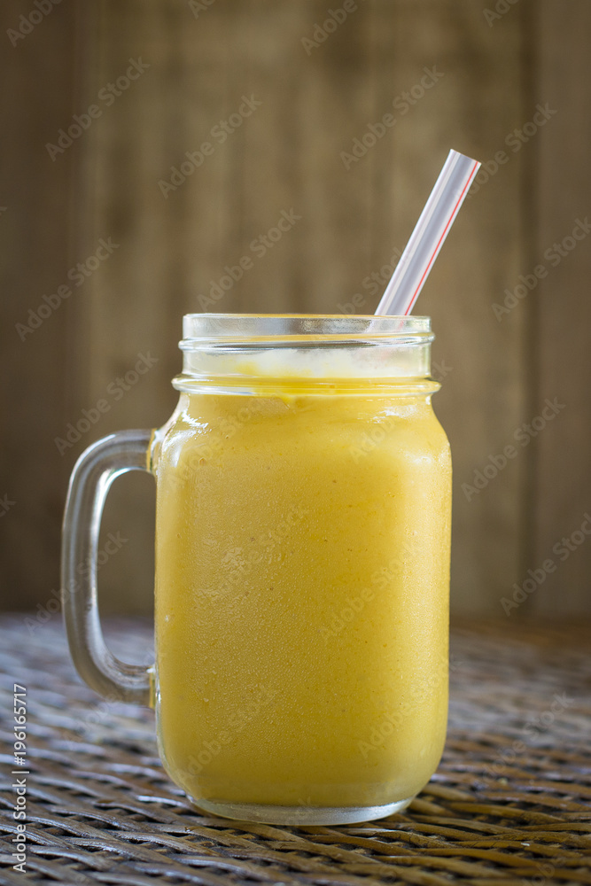 Fresh organic mango shake in glass mug on wooden table, close up Fresh organic mango shake in glass mug on wooden table, close up