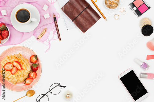 Beautiful flatlay arrangement with cup of coffee, hot waffles with cream and strawberries, smartphone with copyspace and beauty accessories: concept of busy morning breakfast, white background. photo