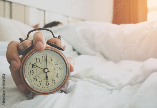 Man stretched in bed after the alarm clock 6 AM in the sunlight morning.