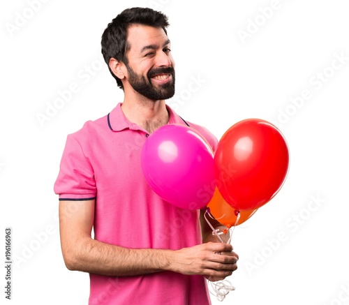 Handsome young man holding balloons and  winking over isolated white background © luismolinero