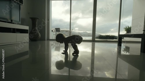 Baby child falling down during learning to walk on floor in bright apartment