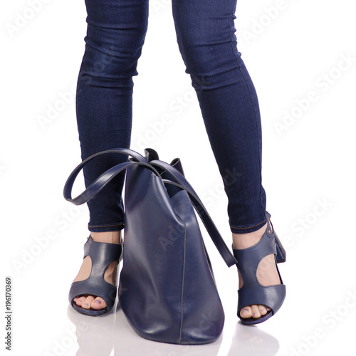 Female legs in jeans and in blue sandals shoes with blue leather bag handbag