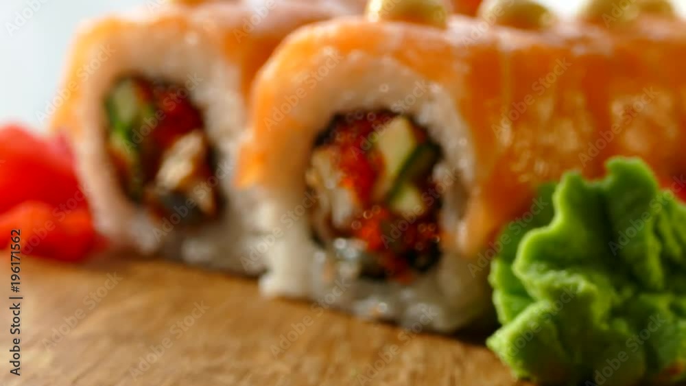 Tasty and appetizing sushi. Sushi with slices of salmon and fresh cucumbers. Red ginger and green wasabi on a wooden board were served to sushi. Sushi red dragon