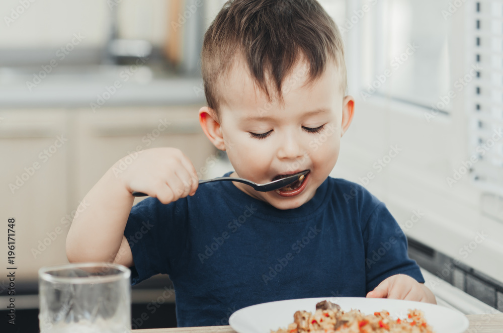 beautiful cute baby eats rice with a spoon in the kitchen, very fun beautiful cute baby eats rice with a spoon in the kitchen, very fun