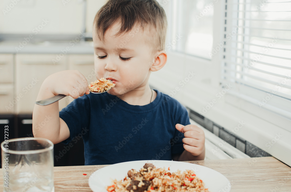 beautiful cute baby eats rice with a spoon in the kitchen, very fun beautiful cute baby eats rice with a spoon in the kitchen, very fun