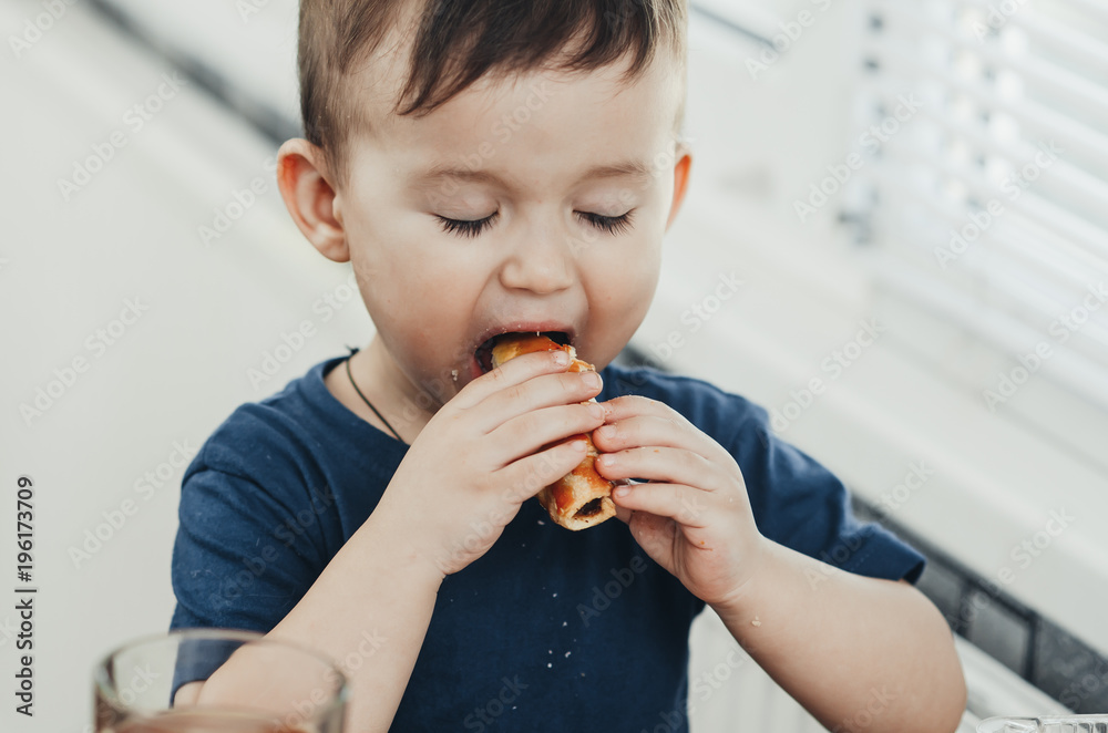 Beautiful baby sitting in the kitchen eating a delicious tube of condensed milk