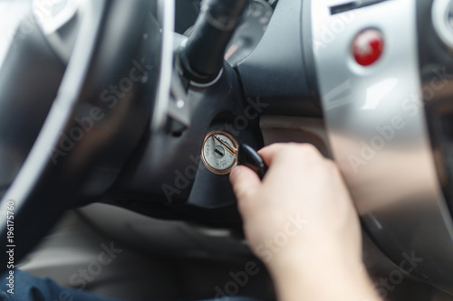 Hand s man plug in a key starting the engine of a car. The hand inserts the key into the ignition and starts the car. Hand put the car key to the keyhole starting the car.