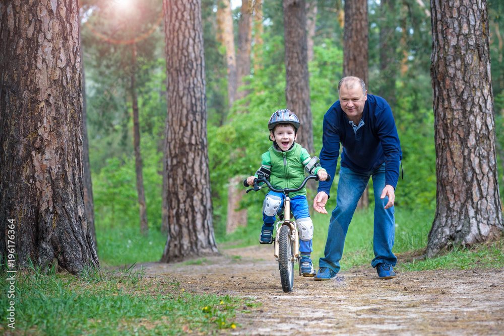 Little kid boy of 3 years and his father in autumn forest with a bicycle. Dad teaching his son. Man happy about success. Child with helmet. Safety, sports, leisure with kids concept. Little kid boy of 3 years and his father in autumn forest with a bicycle. Dad teaching his son. Man happy about success. Child with helmet. Safety, sports, leisure with kids concept.