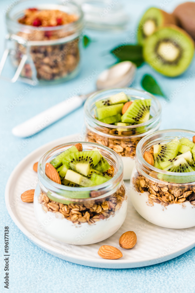 Fruit dessert, kiwi granola parfait with nuts and greek yogurt in glass jars. Selective focus, space for text. Fruit dessert, kiwi granola parfait with nuts and greek yogurt in glass jars. Selective focus, space for text.