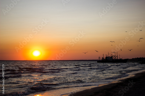 Golden natural sea sunset view of the pier or small bridge on the horizon and orange sky landscape. Sunset or sunrise in nature with the sun in the clouds above the black seascapes.