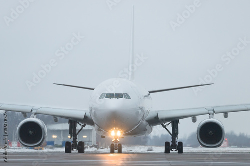 Closeup of passenger wide-body plane rides after landing in twilight, front view, winter time. Included landing lights at the aircraft. Aviation concept