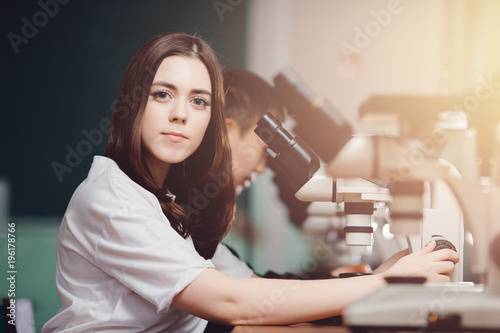 Student girl looks through microscope in an equipped classroom with series of microscopes. The concept is to study science of biology  organisms  bacteria  viruses.