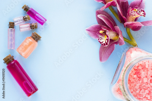 Spa and wellness setting with orchid and rose sea salt and bottles with oil on blue background copyspace