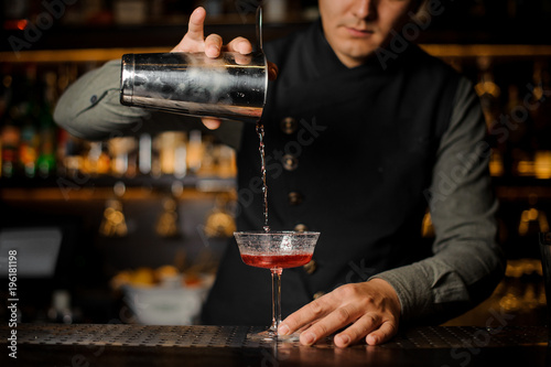 Barman pouring alcoholic drink with campari into the cocktail glass