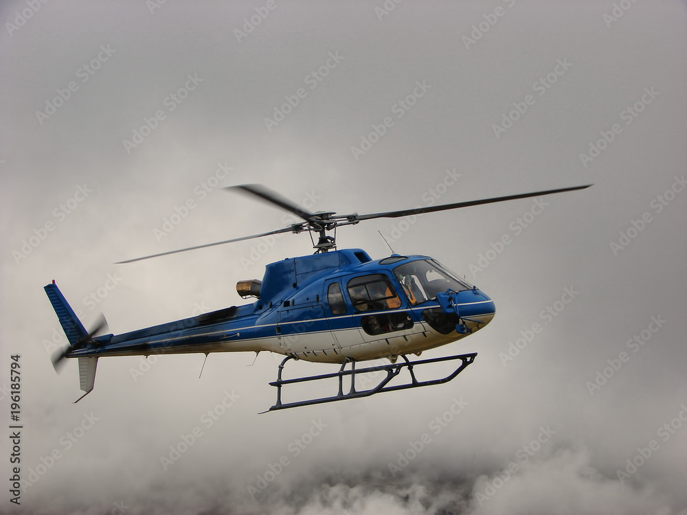 Blue helicopter flying in clouds