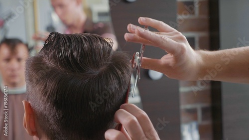 Close-up of barber cuts the hair by scissors at barbershop.